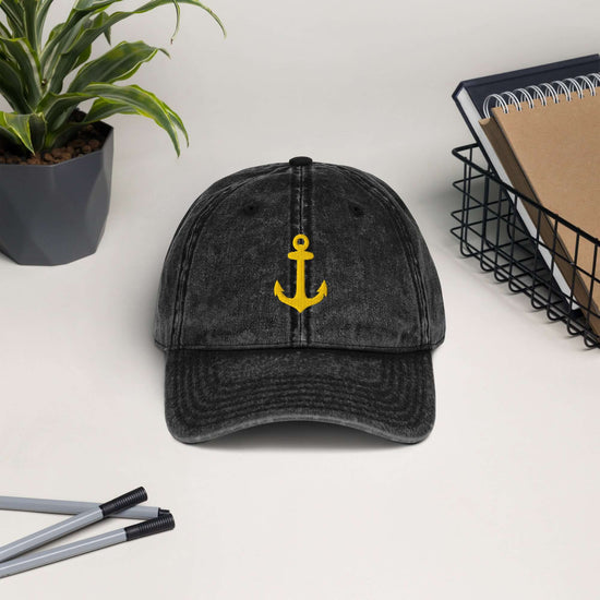 Vintage cotton twill cap with yellow anchor embroidery on a desk with plants and office supplies.
